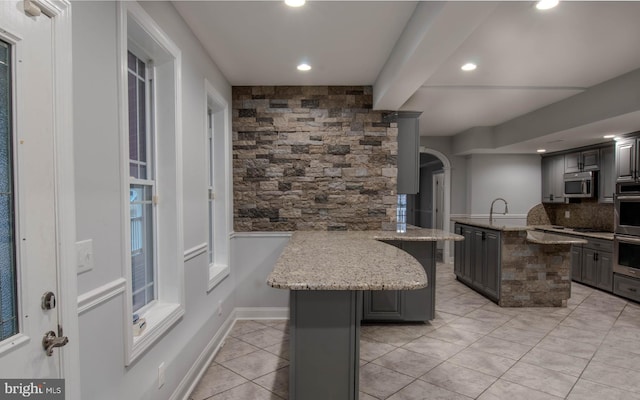 kitchen with a kitchen island, appliances with stainless steel finishes, backsplash, kitchen peninsula, and light stone countertops