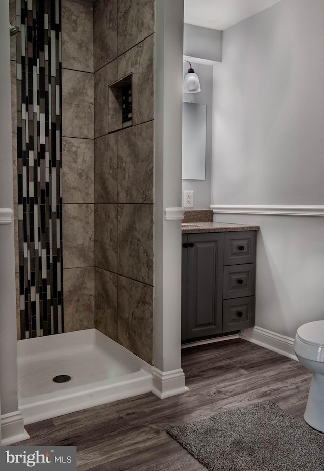 bathroom featuring a tile shower, hardwood / wood-style floors, vanity, and toilet