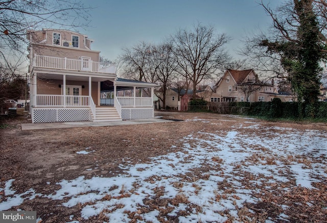 snow covered house featuring a porch and a balcony