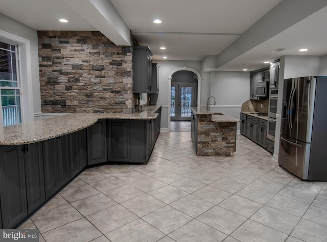 kitchen with sink, appliances with stainless steel finishes, light stone counters, tasteful backsplash, and kitchen peninsula