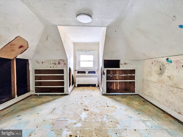 interior space with vaulted ceiling, a textured ceiling, and radiator heating unit