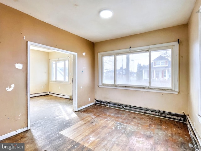 spare room featuring a baseboard heating unit, baseboards, and wood finished floors