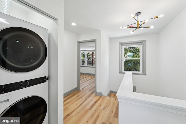 laundry area featuring stacked washer and dryer, a notable chandelier, and light hardwood / wood-style flooring