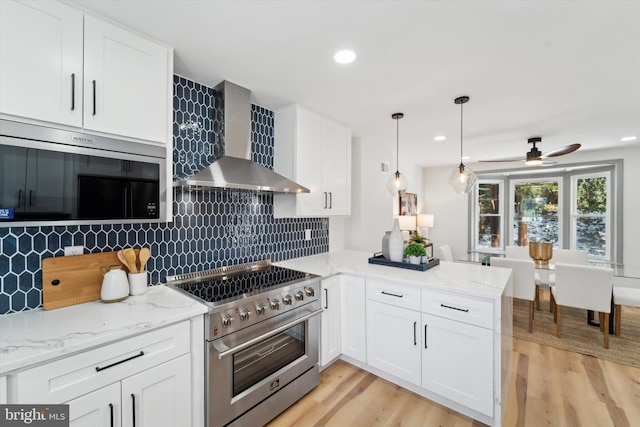 kitchen with wall chimney exhaust hood, white cabinetry, appliances with stainless steel finishes, kitchen peninsula, and backsplash