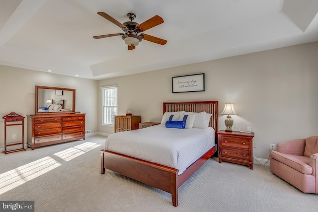 bedroom featuring a tray ceiling, light colored carpet, and ceiling fan