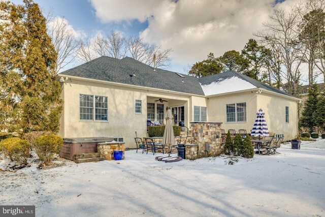 snow covered back of property featuring ceiling fan and a hot tub