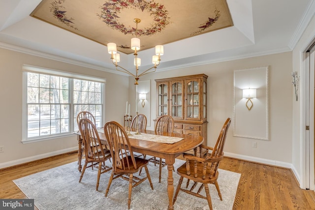 dining area with an inviting chandelier, ornamental molding, a tray ceiling, and light wood-type flooring