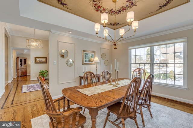 dining room with crown molding, a tray ceiling, light wood-type flooring, and a notable chandelier