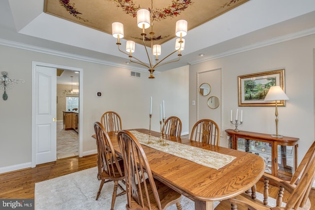 dining space featuring an inviting chandelier, ornamental molding, a raised ceiling, and wood-type flooring