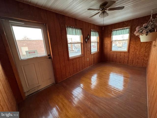 unfurnished room featuring wood-type flooring, a wealth of natural light, ceiling fan, and wooden walls