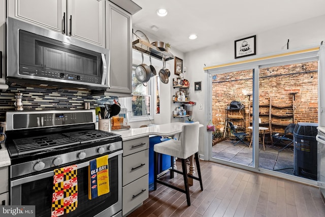 kitchen with gray cabinetry, light stone counters, appliances with stainless steel finishes, dark hardwood / wood-style floors, and decorative backsplash