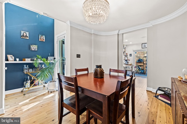 dining area with crown molding, an inviting chandelier, and light hardwood / wood-style flooring