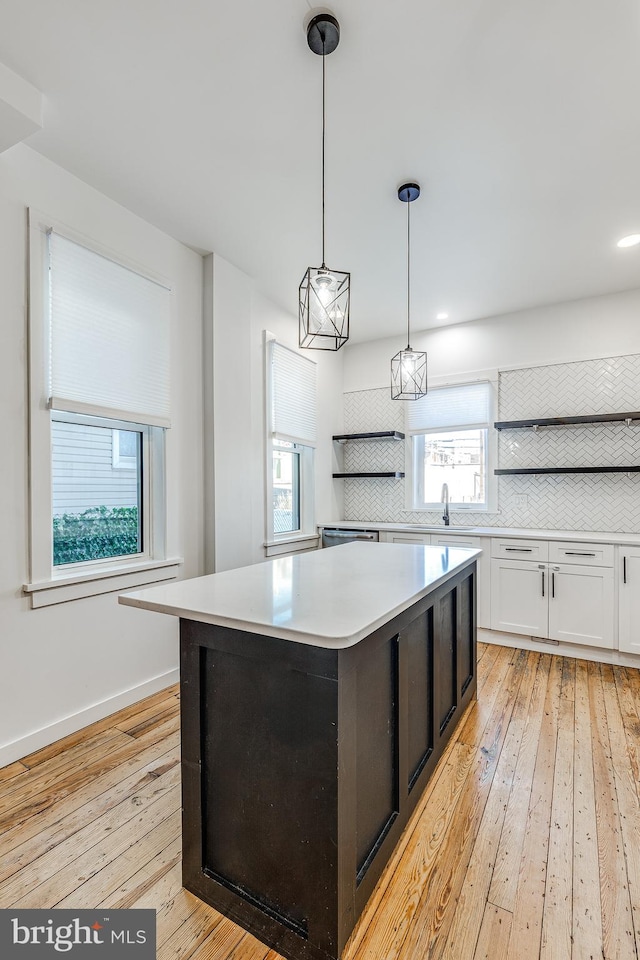 kitchen with white cabinets, decorative backsplash, hanging light fixtures, a center island, and light wood-type flooring