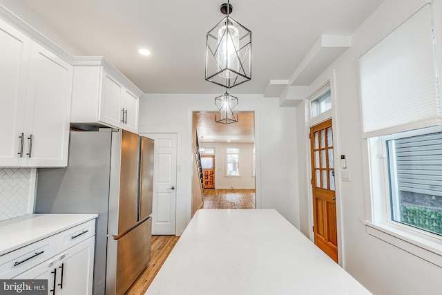 kitchen with stainless steel fridge, tasteful backsplash, white cabinets, decorative light fixtures, and light wood-type flooring