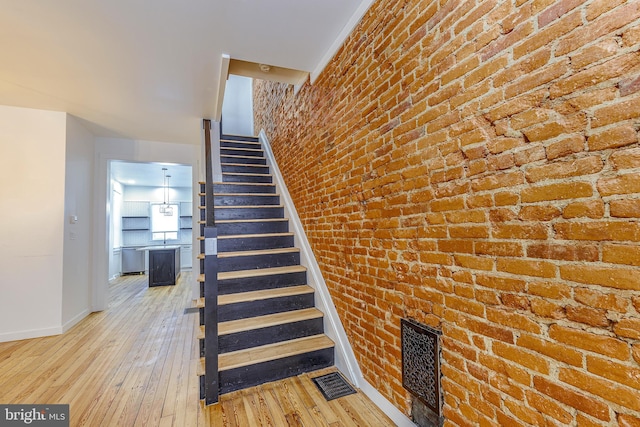 staircase with wood-type flooring and brick wall