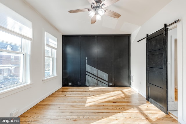 unfurnished bedroom with multiple windows, a barn door, ceiling fan, and light hardwood / wood-style flooring