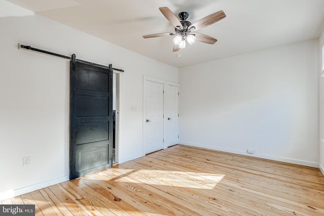 unfurnished bedroom with ceiling fan, a barn door, a closet, and light wood-type flooring