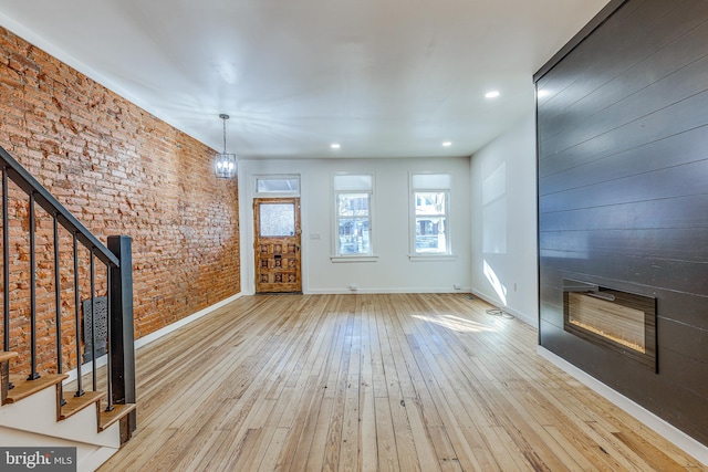 unfurnished living room featuring brick wall, a chandelier, and light wood-type flooring