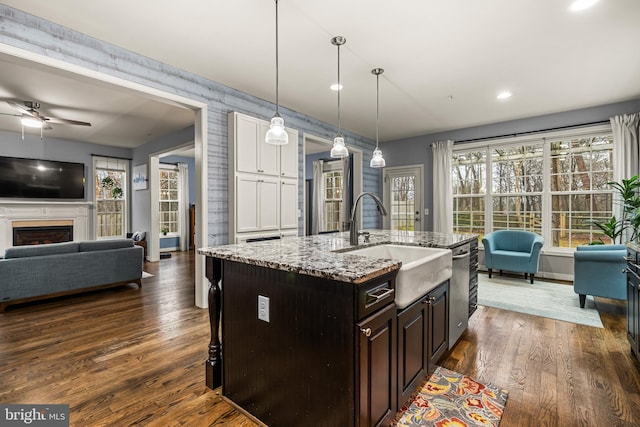 kitchen featuring pendant lighting, sink, dark brown cabinetry, a center island with sink, and dark hardwood / wood-style flooring