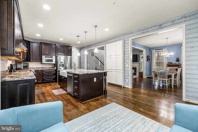 kitchen with dark brown cabinetry, appliances with stainless steel finishes, dark hardwood / wood-style flooring, pendant lighting, and a kitchen island with sink