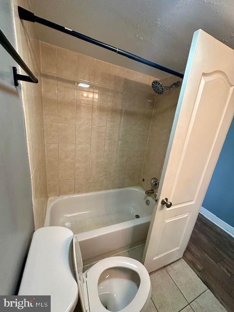 bathroom featuring tile patterned flooring, tiled shower / bath combo, and toilet