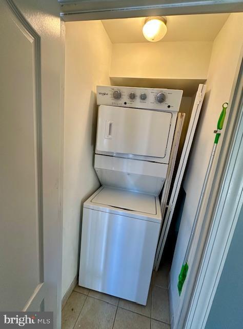 clothes washing area with stacked washer / drying machine and light tile patterned floors