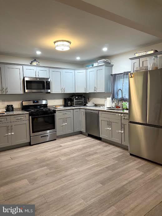 kitchen featuring appliances with stainless steel finishes, light wood-type flooring, a sink, and gray cabinetry