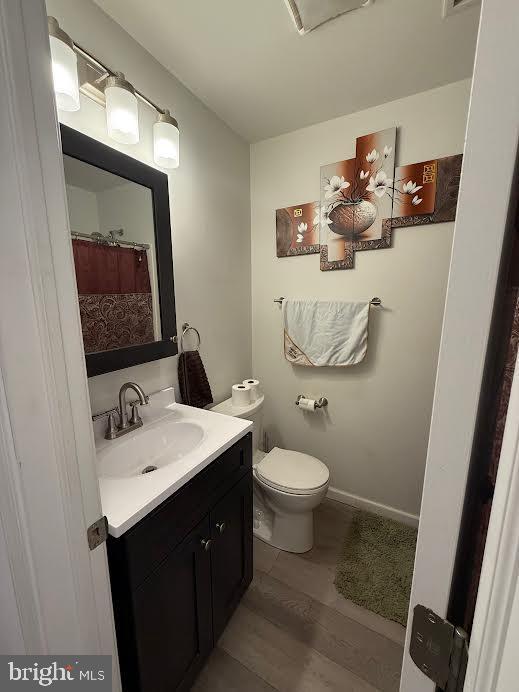 full bathroom with toilet, wood finished floors, vanity, and baseboards