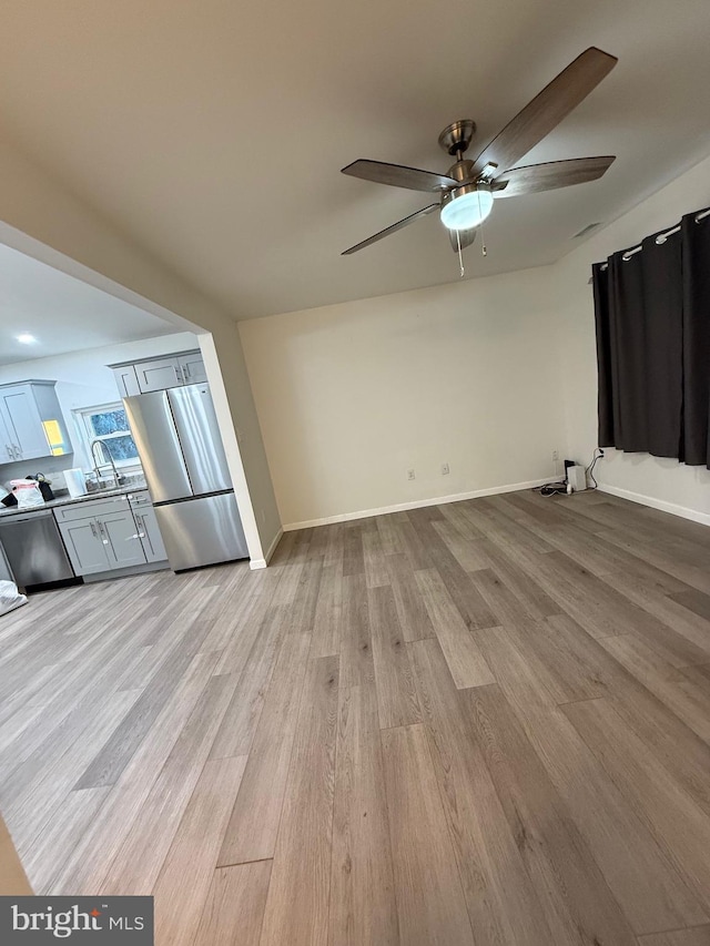 unfurnished living room with a ceiling fan, light wood-style flooring, and baseboards