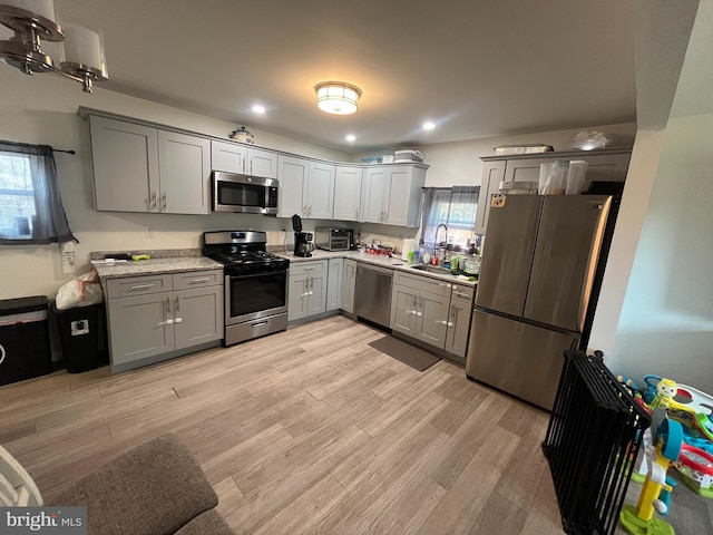 kitchen with a sink, stainless steel appliances, light wood finished floors, and gray cabinets