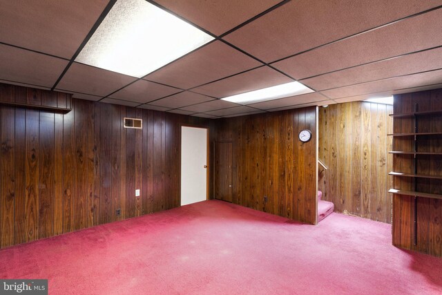 basement with a paneled ceiling, light carpet, and wood walls