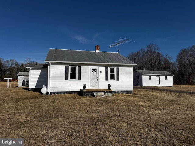 view of front facade featuring a front yard, a standing seam roof, metal roof, and a chimney