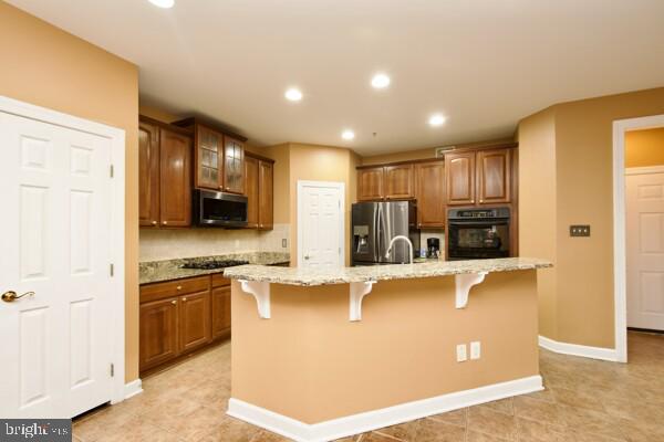 kitchen featuring light stone counters, a kitchen bar, black appliances, and a center island with sink