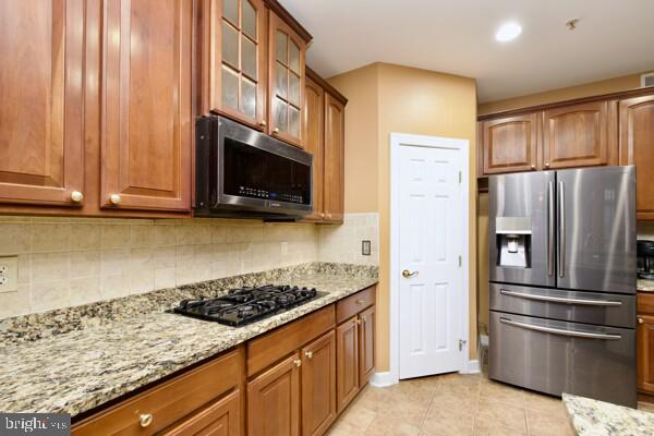 kitchen featuring stainless steel appliances, tasteful backsplash, light tile patterned floors, and light stone counters