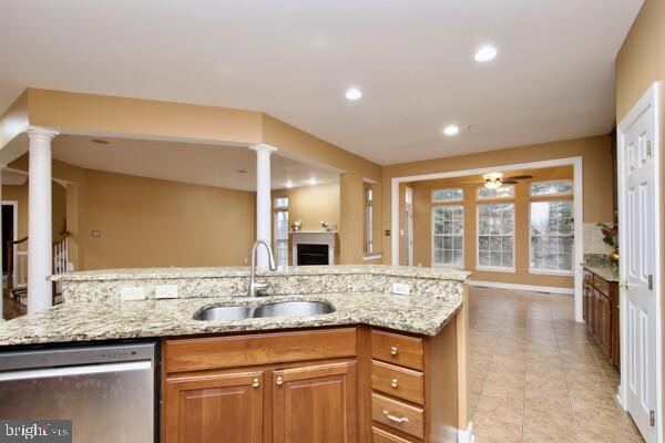 kitchen featuring light stone counters, sink, stainless steel dishwasher, and decorative columns