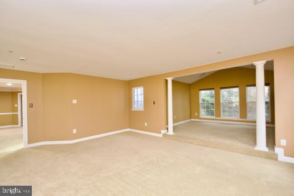 carpeted empty room featuring lofted ceiling and ornate columns