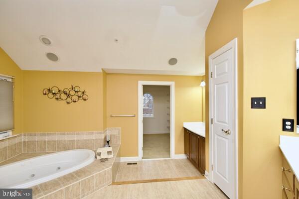 bathroom featuring vanity, vaulted ceiling, and tiled bath