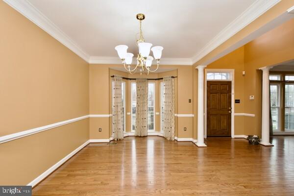 entryway featuring crown molding, a chandelier, decorative columns, and hardwood / wood-style floors