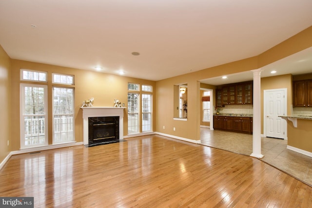 unfurnished living room featuring a healthy amount of sunlight, a premium fireplace, decorative columns, and light hardwood / wood-style flooring