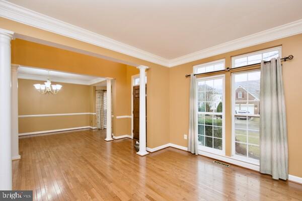 unfurnished room with a notable chandelier, crown molding, wood-type flooring, and decorative columns