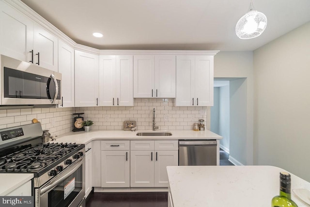 kitchen with light countertops, hanging light fixtures, appliances with stainless steel finishes, white cabinets, and a sink