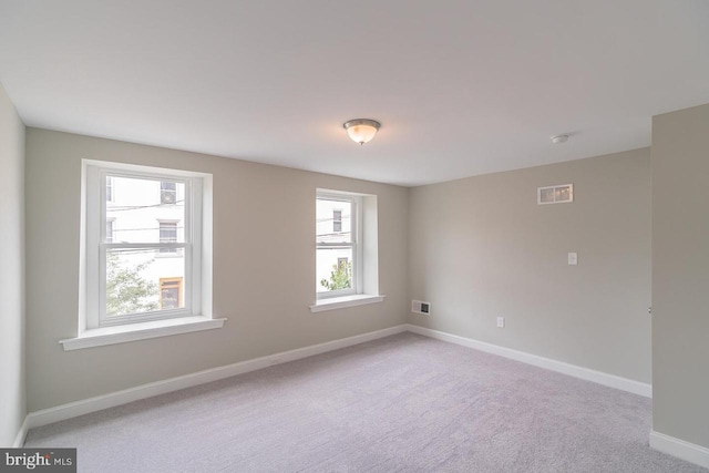 empty room featuring visible vents, light carpet, and baseboards