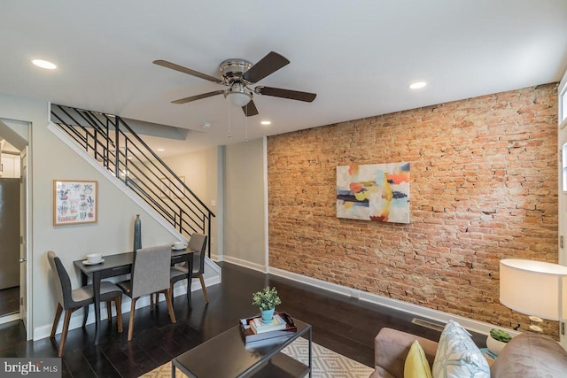 living area featuring baseboards, dark wood finished floors, brick wall, stairway, and recessed lighting