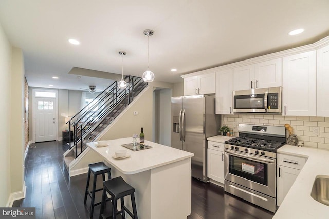 kitchen with appliances with stainless steel finishes, a center island, decorative light fixtures, light countertops, and white cabinetry