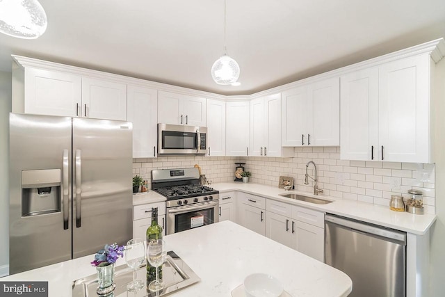 kitchen featuring white cabinets, appliances with stainless steel finishes, decorative light fixtures, light countertops, and a sink