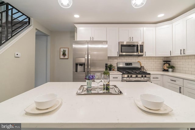 kitchen with tasteful backsplash, appliances with stainless steel finishes, light stone counters, and white cabinets