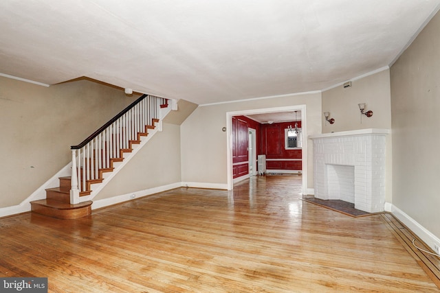 unfurnished living room featuring hardwood / wood-style flooring, crown molding, radiator, and a brick fireplace