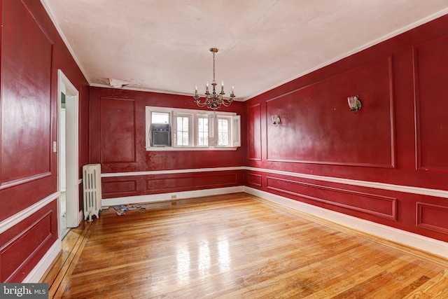 unfurnished dining area with crown molding, radiator, hardwood / wood-style floors, and an inviting chandelier