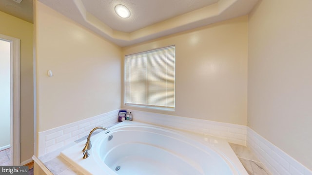 bathroom with a raised ceiling, a textured ceiling, and tiled tub