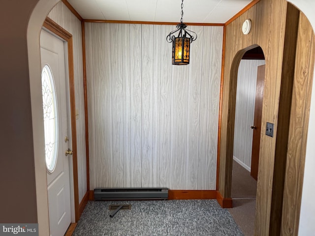 foyer featuring crown molding, a baseboard heating unit, dark carpet, and wood walls